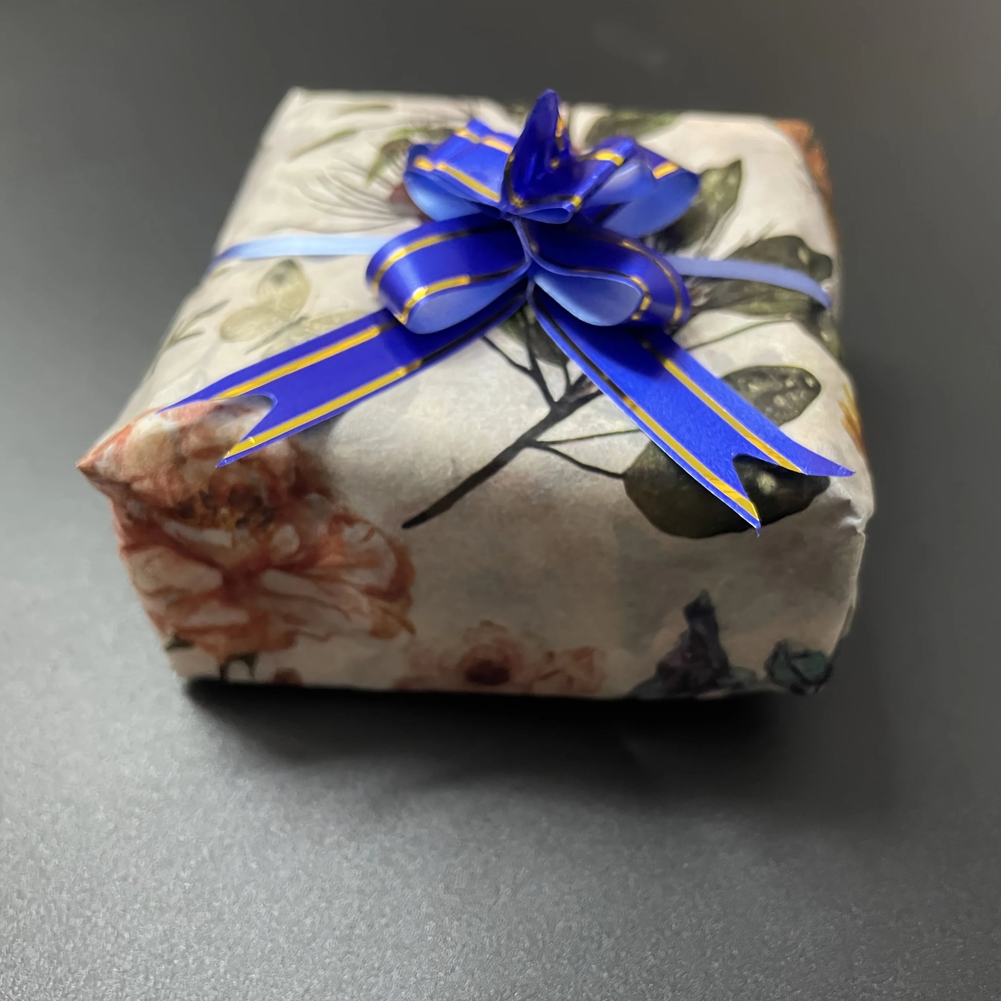 Gift box wrapped in floral paper with a blue ribbon on a gray background