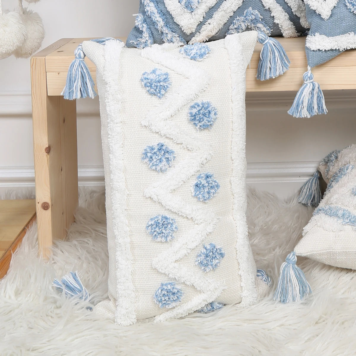 Decorative pillow with blue pom-poms and tassels on a wooden bench.