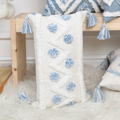 Decorative pillow with blue pom-poms and tassels on a wooden bench.