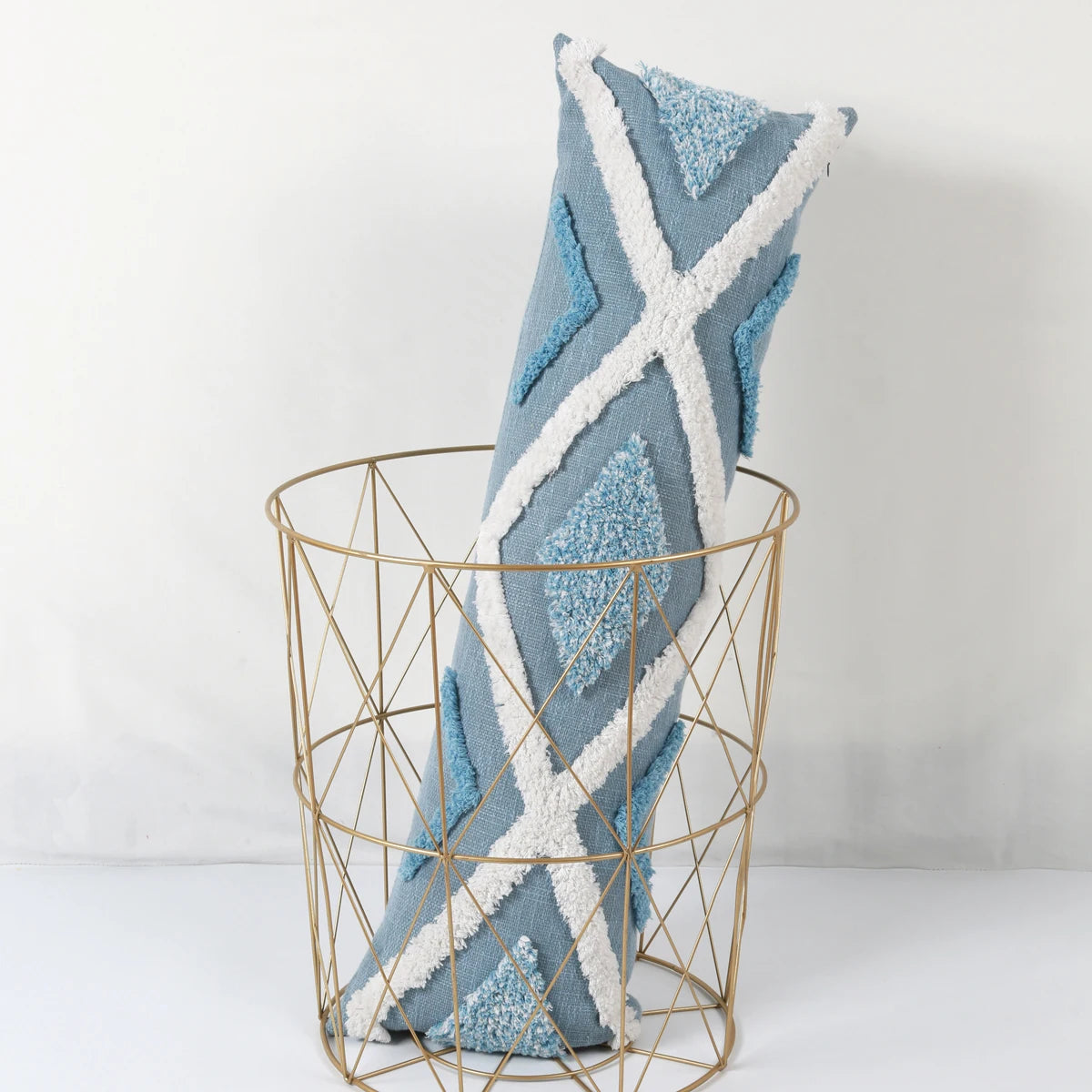 Decorative pillow with blue and white pattern in a gold wire basket on a white background