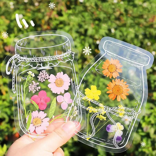 Transparent stickers of mason jars with flowers held against a green leafy background
