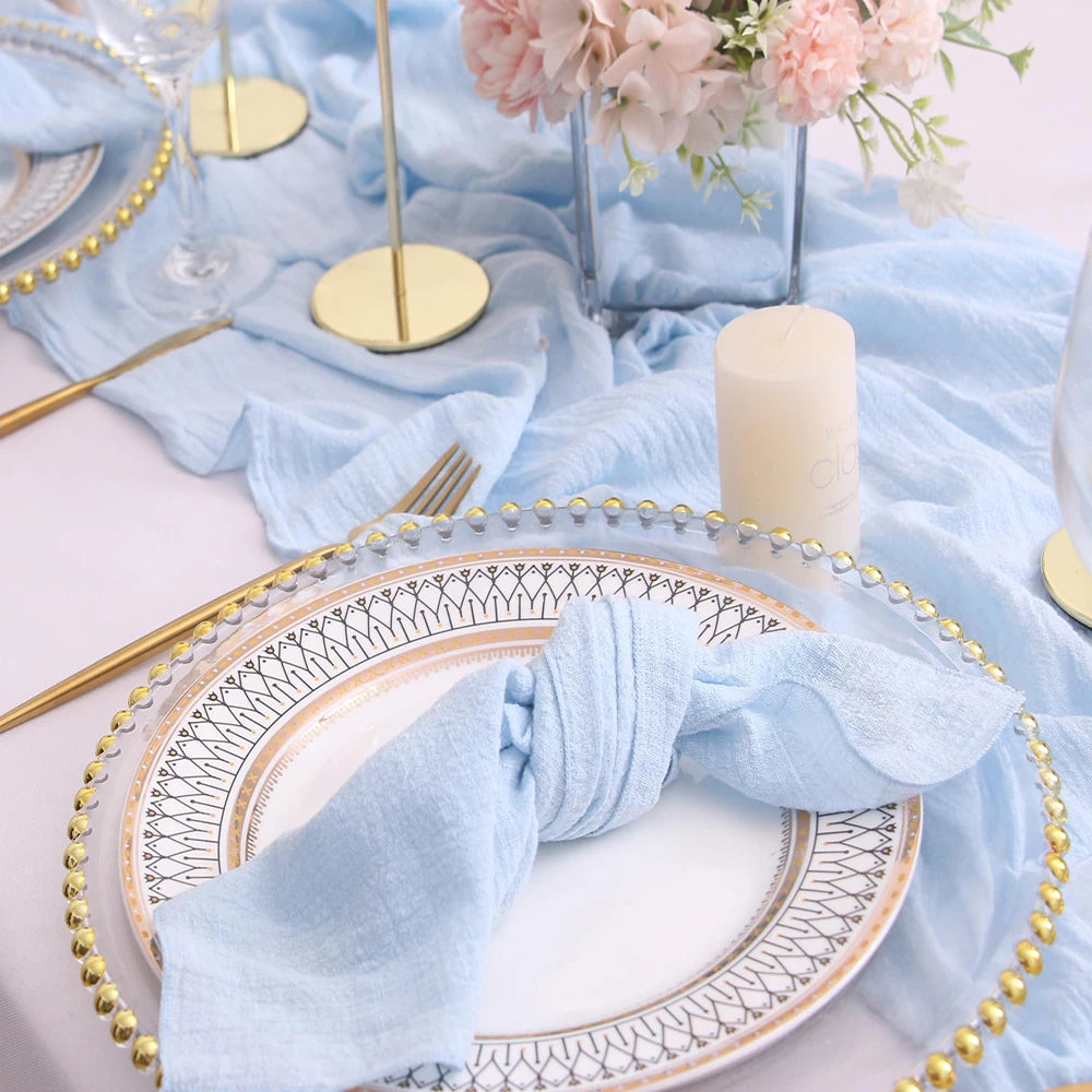 Elegant table setting with light blue napkins, gold cutlery, and floral centerpiece.