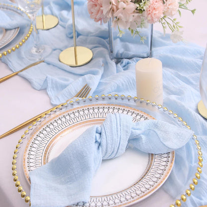 Elegant table setting with light blue napkins, gold cutlery, and floral centerpiece.