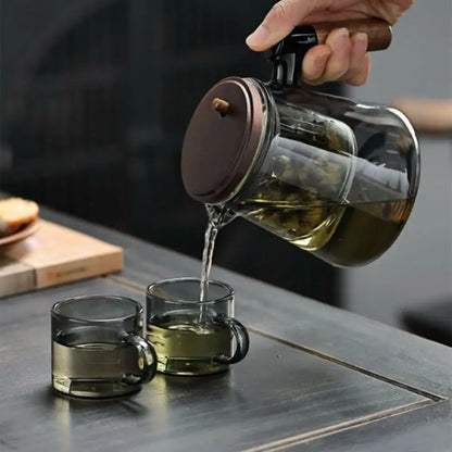 Glass teapot being poured into two cups on a wooden surface
