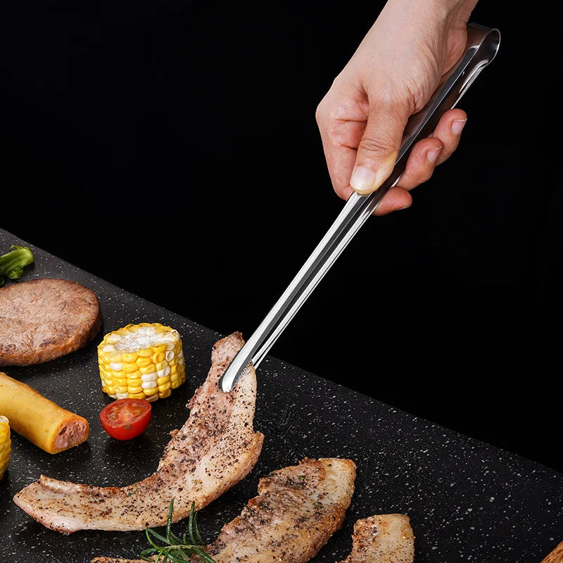 Hand using tongs to handle grilled food on a black surface