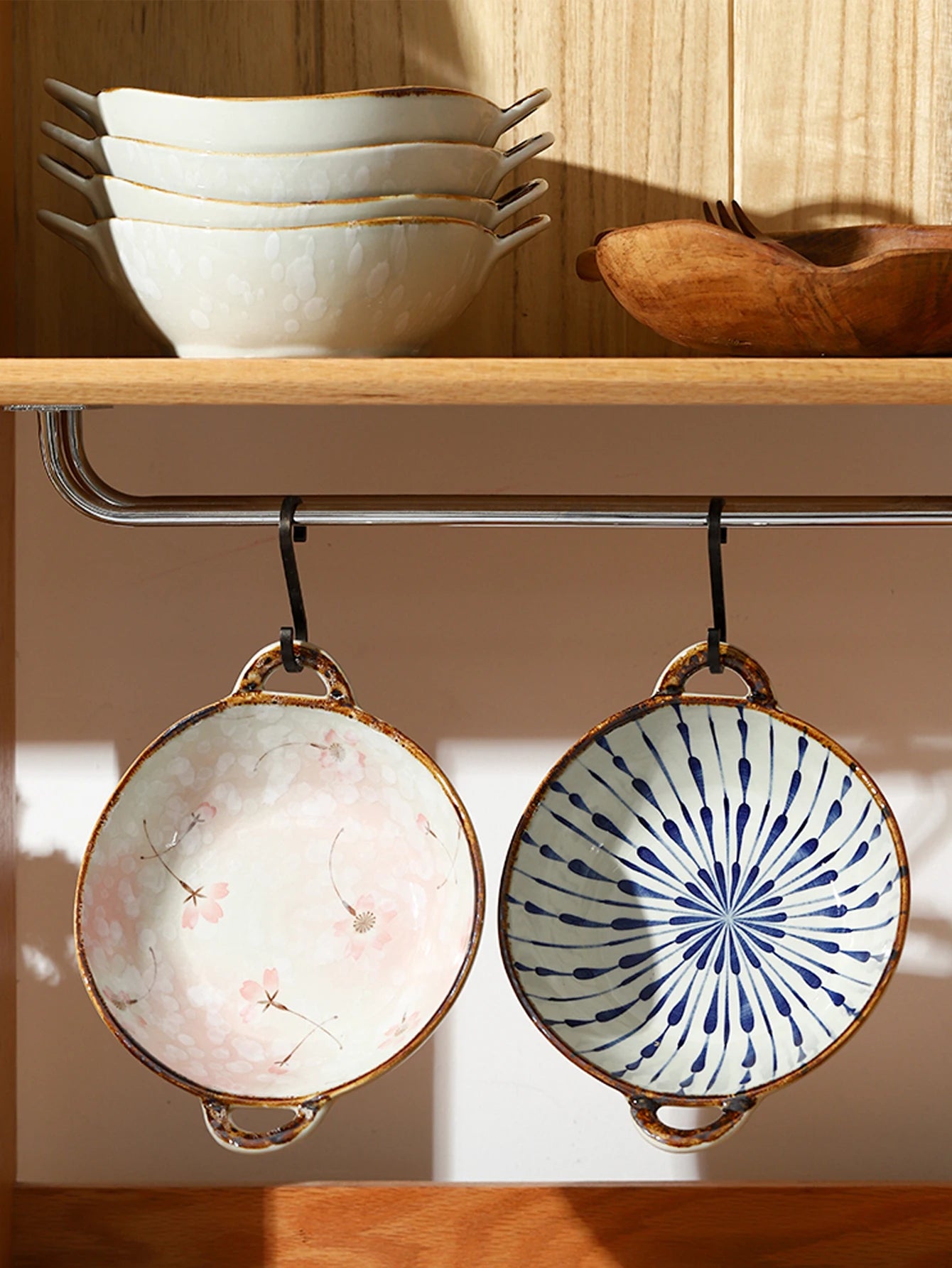 Two ceramic bowls with decorative patterns hanging from a hook on a wooden shelf.