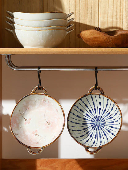 Two ceramic bowls with decorative patterns hanging from a hook on a wooden shelf.