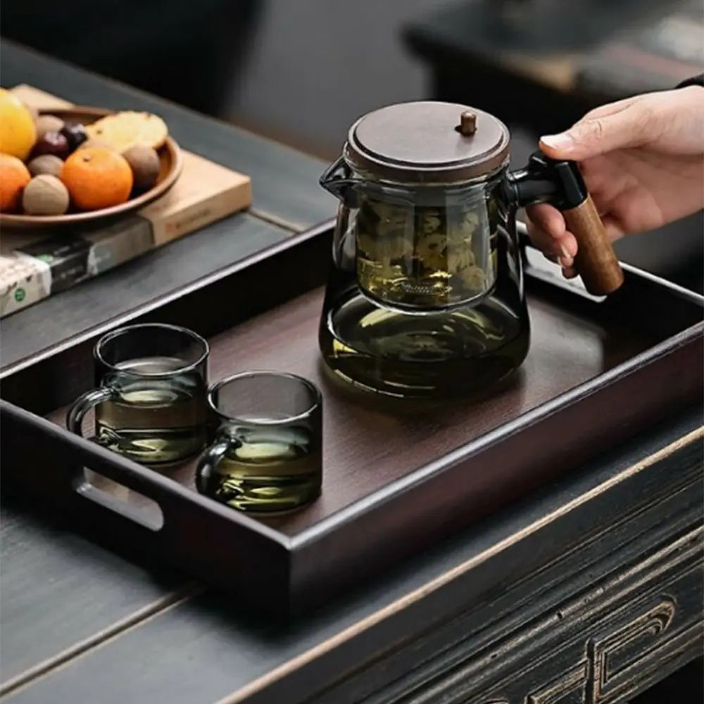 Tea-making setup with glass teapot and cups on a wooden tray.
