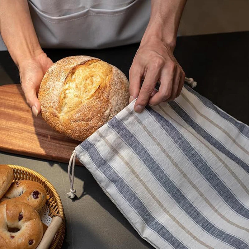 Person holding a loaf of bread with a striped cloth, surrounded by more bread on a wooden board.