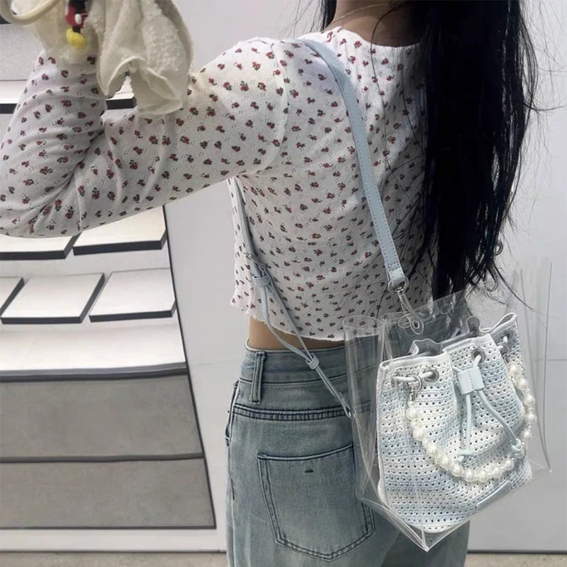 Person wearing a white floral shirt and blue jeans, holding a clear handbag with a white textured pouch.