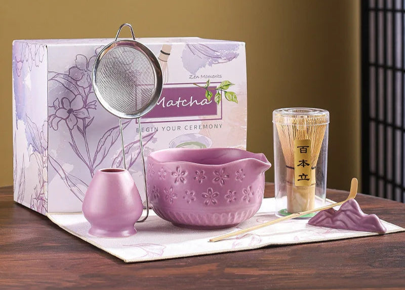 Tea-making set with a purple bowl, strainer, and other items on a wooden surface.