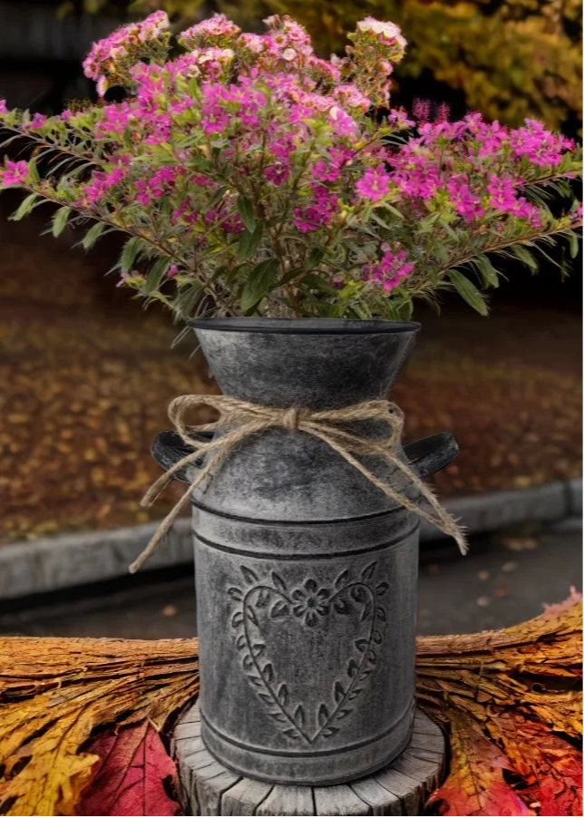 Decorative metal vase with pink flowers on a wooden stump with autumn leaves.