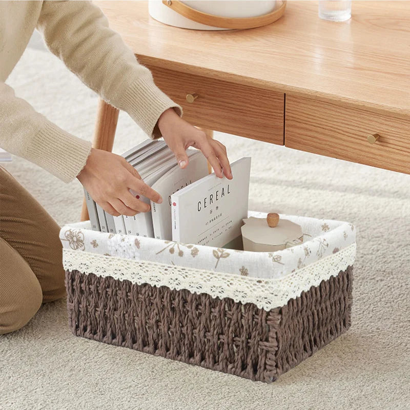 Person organizing books into a decorative storage basket on a carpeted floor.