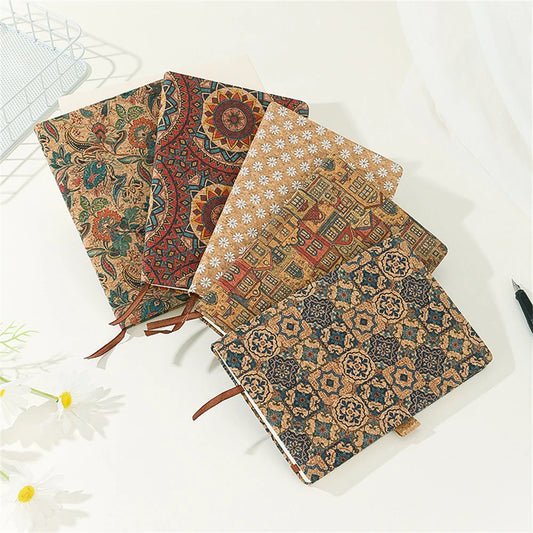 Four patterned notebooks stacked on a white surface with a pen and flowers.