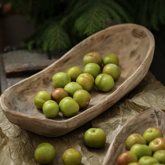 Green fruits in a wooden bowl on a rustic surface with blurred greenery in the background