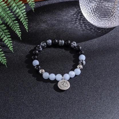 Beaded bracelet with a centralOm symbol charm on a dark surface with ferns and a glass.