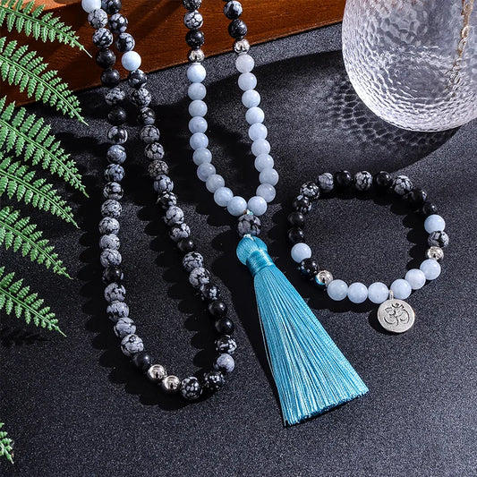 Beaded necklace with tassel and bracelet on a dark surface with green leaves.