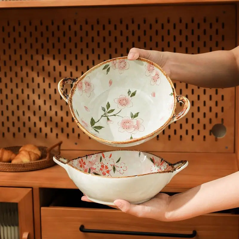 Person holding a floral ceramic bowl with another bowl underneath on a wooden surface.