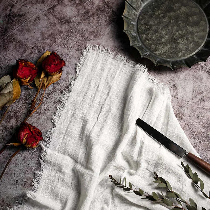 White fabric with a knife, dried roses, and greenery on a textured surface