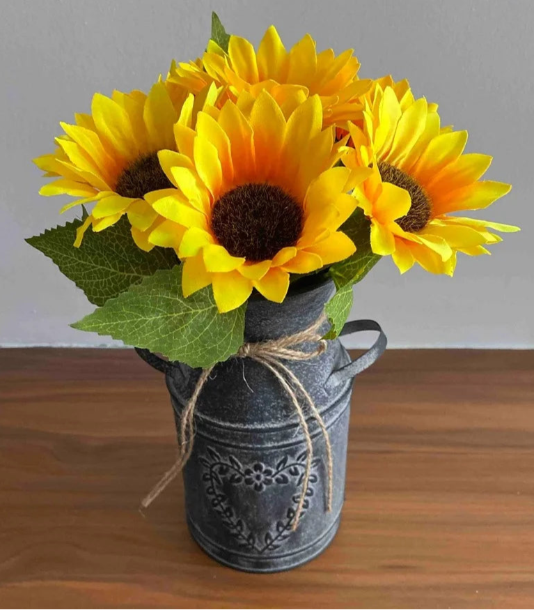 Bouquet of yellow sunflowers in a decorative metal vase on a wooden surface.