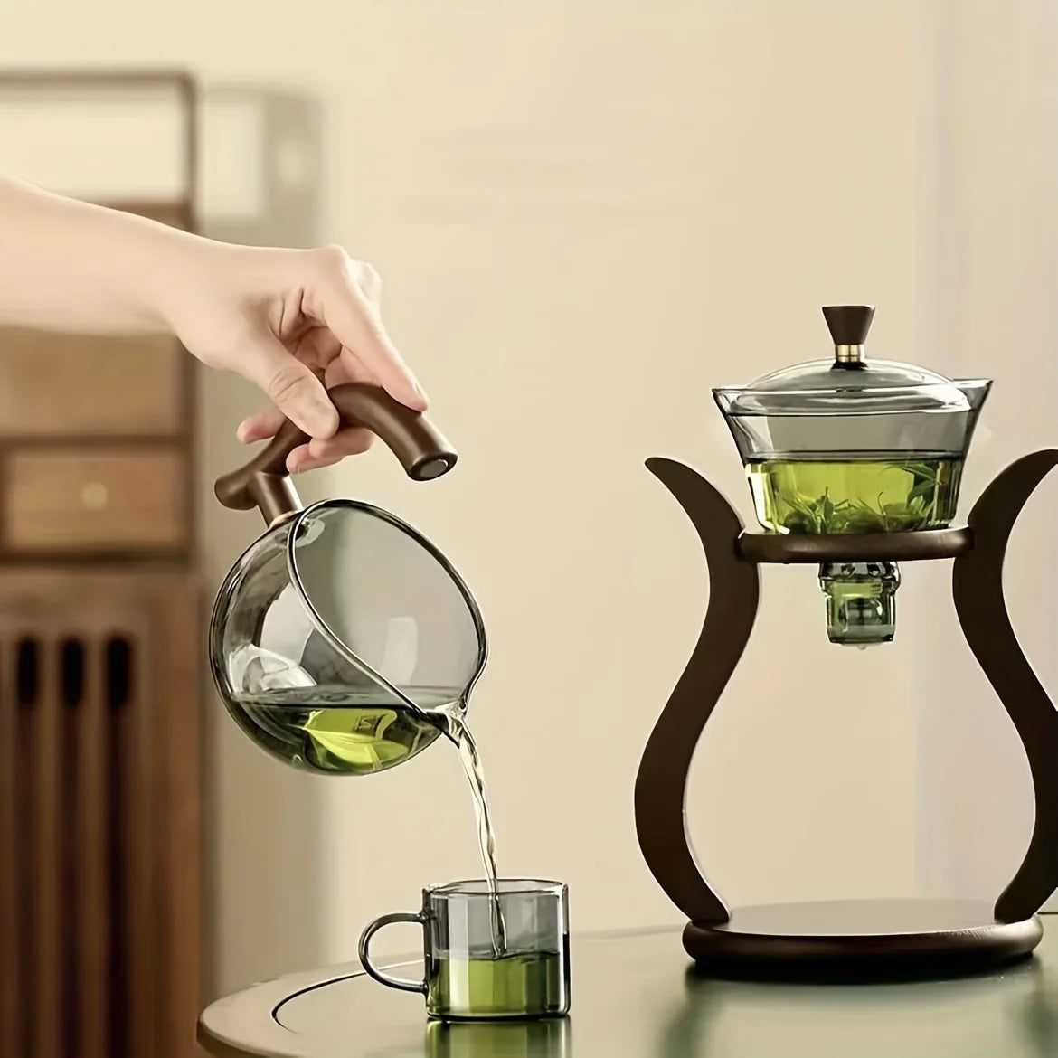 Person pouring green liquid from a glass pitcher into a cup with a wooden handle.