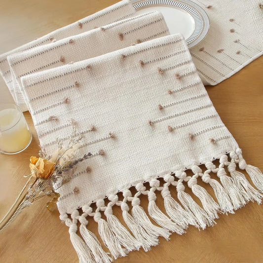 Beige woven placemats with tassels on a wooden table.