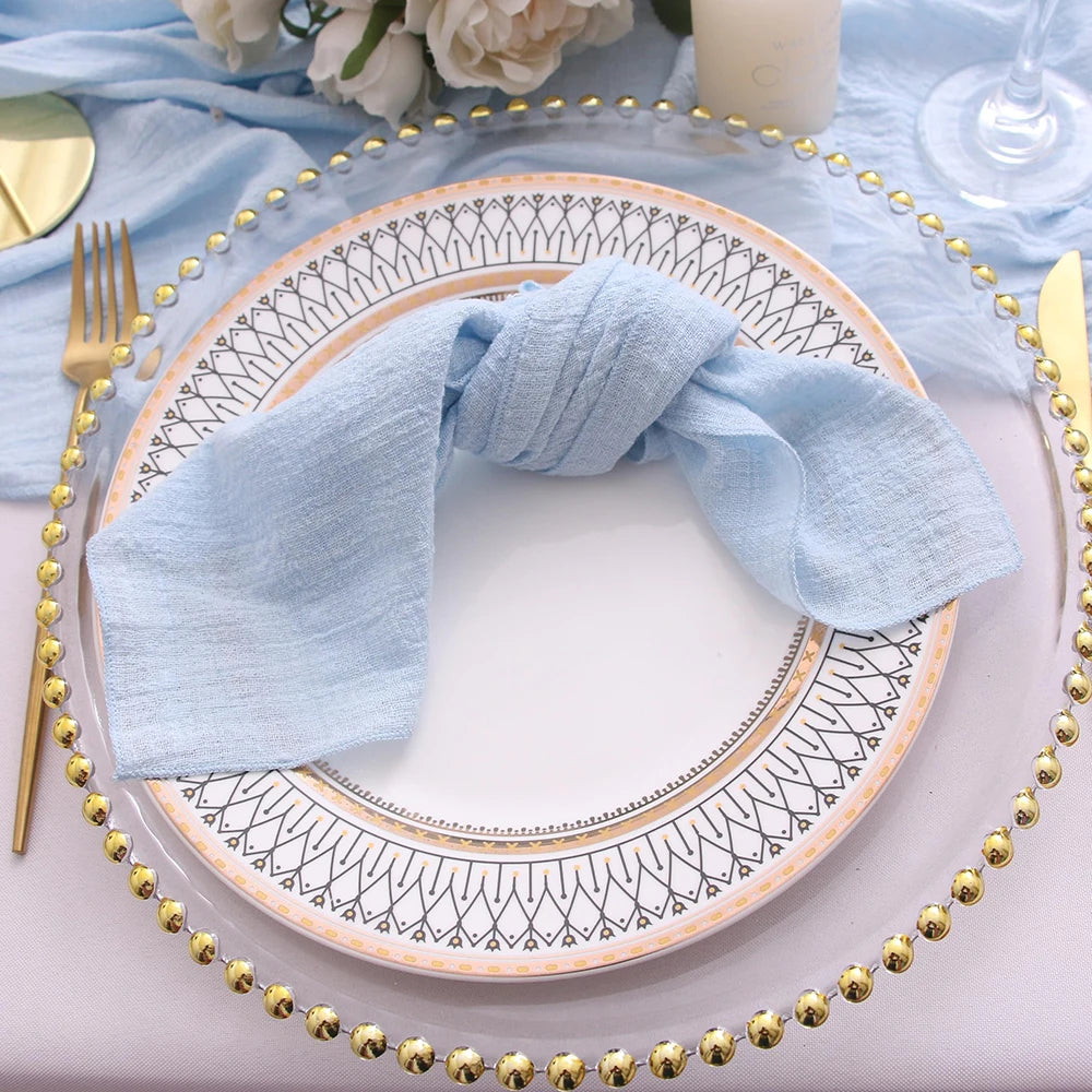 Decorative table setting with a plate, gold beaded runner, and blue napkin.