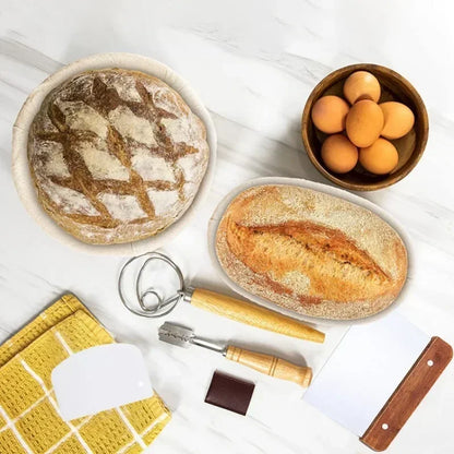 Two loaves of bread, a bowl of eggs, and baking tools on a white surface.
