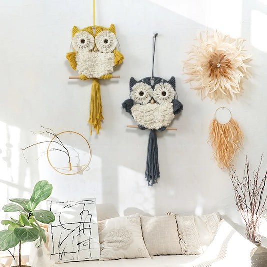 Decorative owl wall hangings on a white wall with a plant and pillows in the foreground.