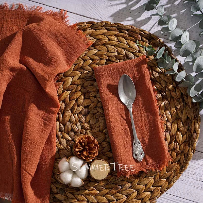 Round woven placemat with orange napkin, silver spoon, and decorative items on a light wooden surface.
