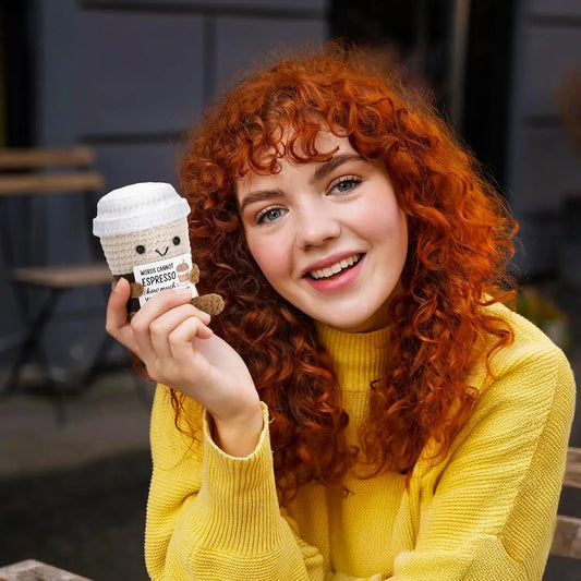 Woman with red hair holding a small coffee cup plush toy outdoors.