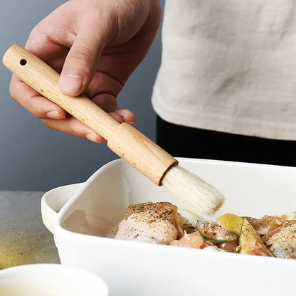 Person using a wooden brush to apply sauce or seasoning to food in a white dish.