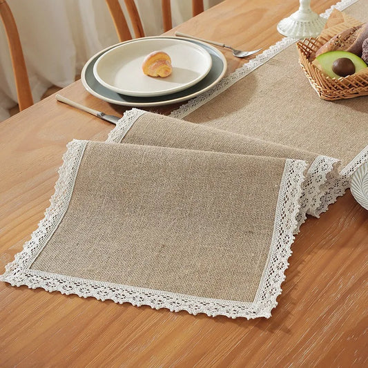 Table setting with burlap placemats and lace trim on a wooden table.