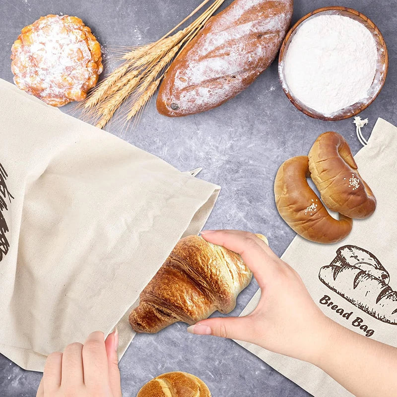 Hand holding a croissant over a bread bag with bread designs on a gray surface with bread and flour.