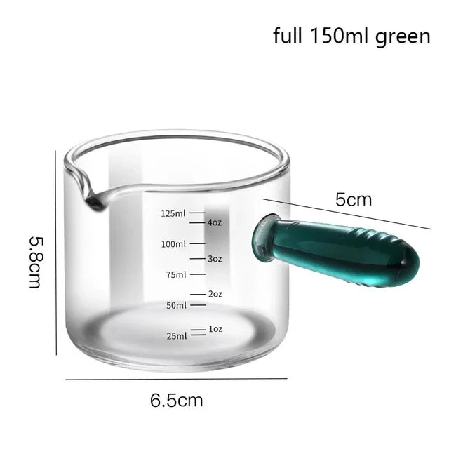 Glass measuring cup with green handle and measurements on a white background