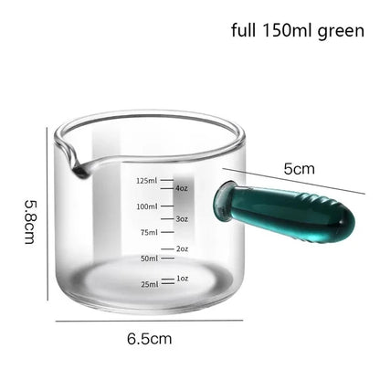 Glass measuring cup with green handle and measurements on a white background