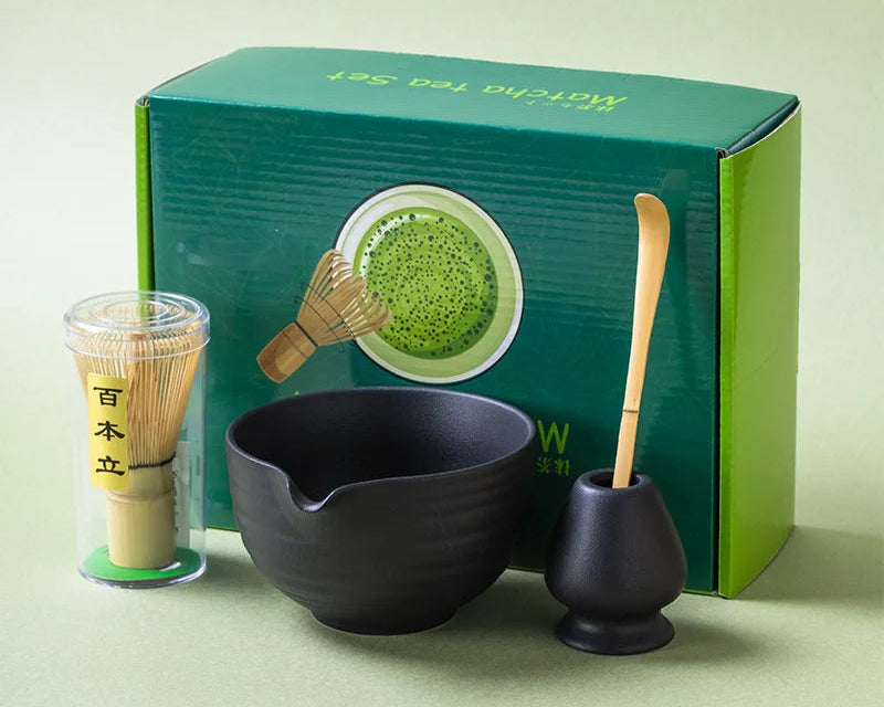 Matcha tea set with black bowl, whisk, and scoop in front of a green box on a light green background