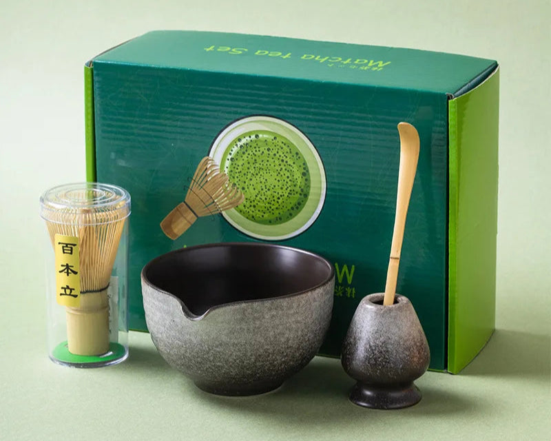 Tea-making set with a bowl, whisk, and scoop in front of a green box on a light green background