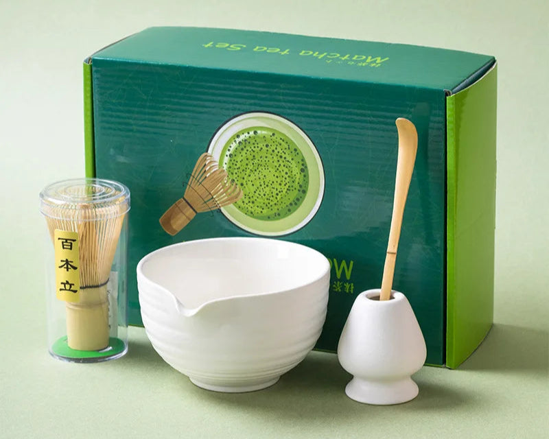 Matcha tea set with bowl, whisk, and holder in front of a green box on a light green background