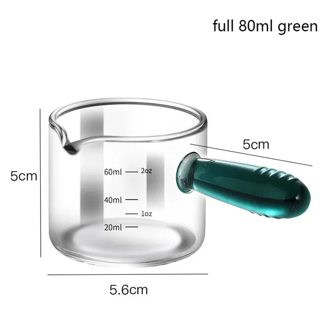 Glass measuring cup with green handle and measurements labeled