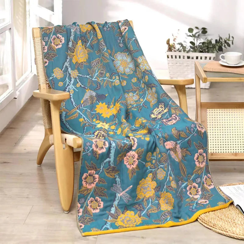 Floral patterned blanket draped over a chair in a room with a table and plants.
