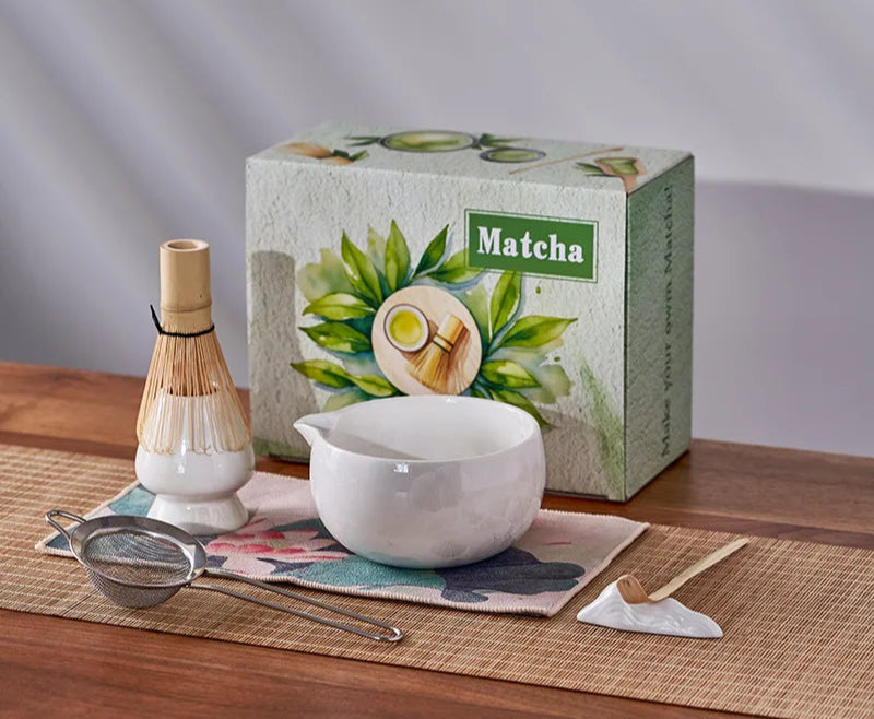 Matcha tea set with box, whisk, bowl, and tools on a wooden surface.