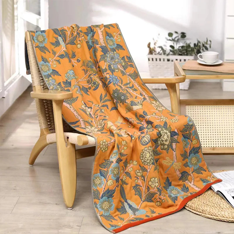 Floral-patterned orange blanket draped over a wooden chair in a bright room.