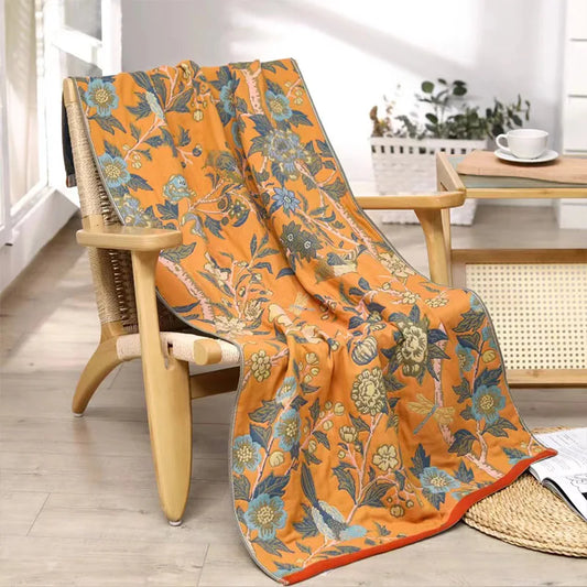 Floral-patterned orange blanket draped over a wooden chair in a bright room.