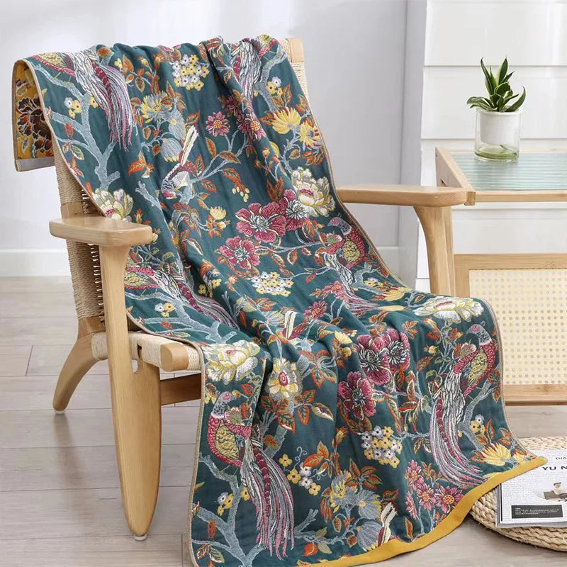 Floral patterned blanket draped over a wooden chair in a room with a table and plant.