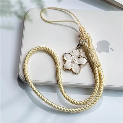 Gold braided phone strap with a floral charm on an Apple device