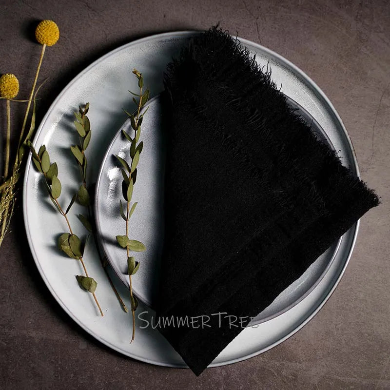 Black napkin on a white plate with greenery and flowers on a dark surface, featuring 'Summer Trees' branding.