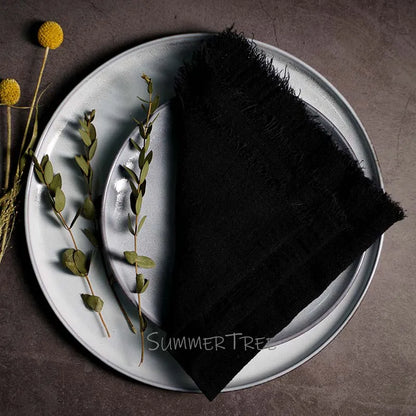 Black napkin on a white plate with greenery and flowers on a dark surface, featuring 'Summer Trees' branding.