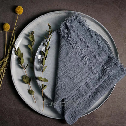Gray napkin on a plate with greenery and a fork, on a brown surface.