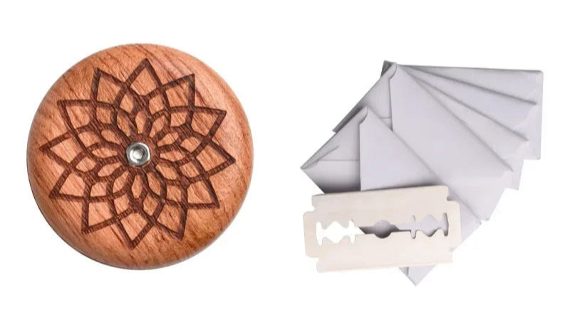 Wooden razor handle with laser-cut design, razor blade, and folded paper on a white background